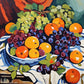 blue and white bowl of oranges and apples with purple and green grapes on a draped white cloth, paint by numbers kit